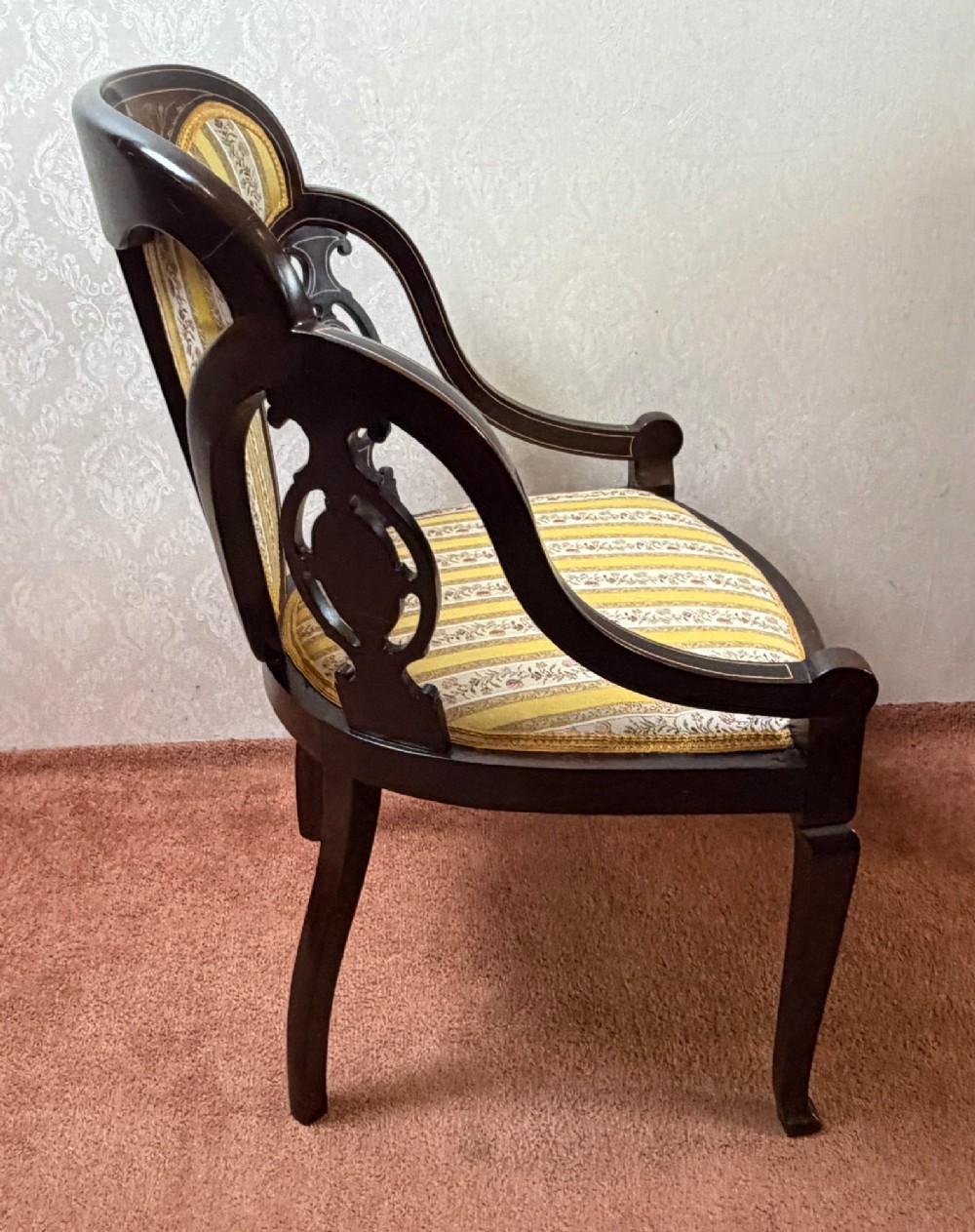 Late 19th century mahogany armchair featuring decorative bone and boxwood urn marquetry, curved arms, and yellow striped floral upholstery. View VI