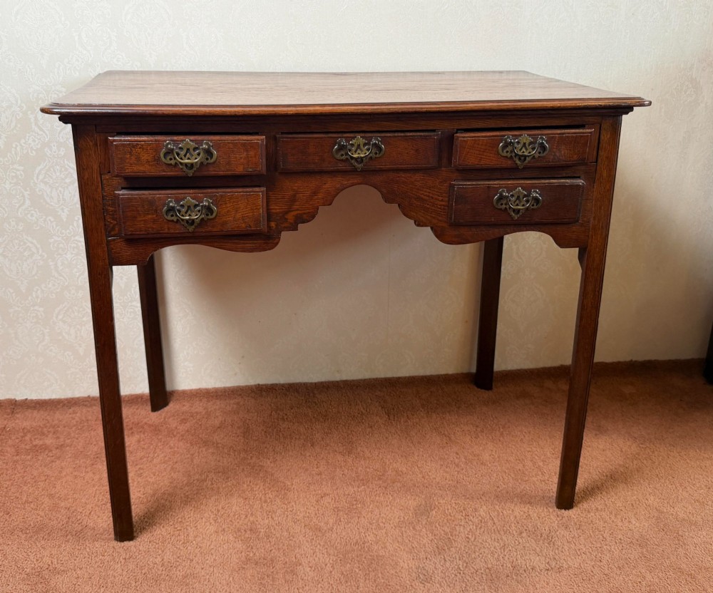 An 18th-century Georgian oak side table featuring five drawers, a central shaped apron, brass handles, and four straight legs.