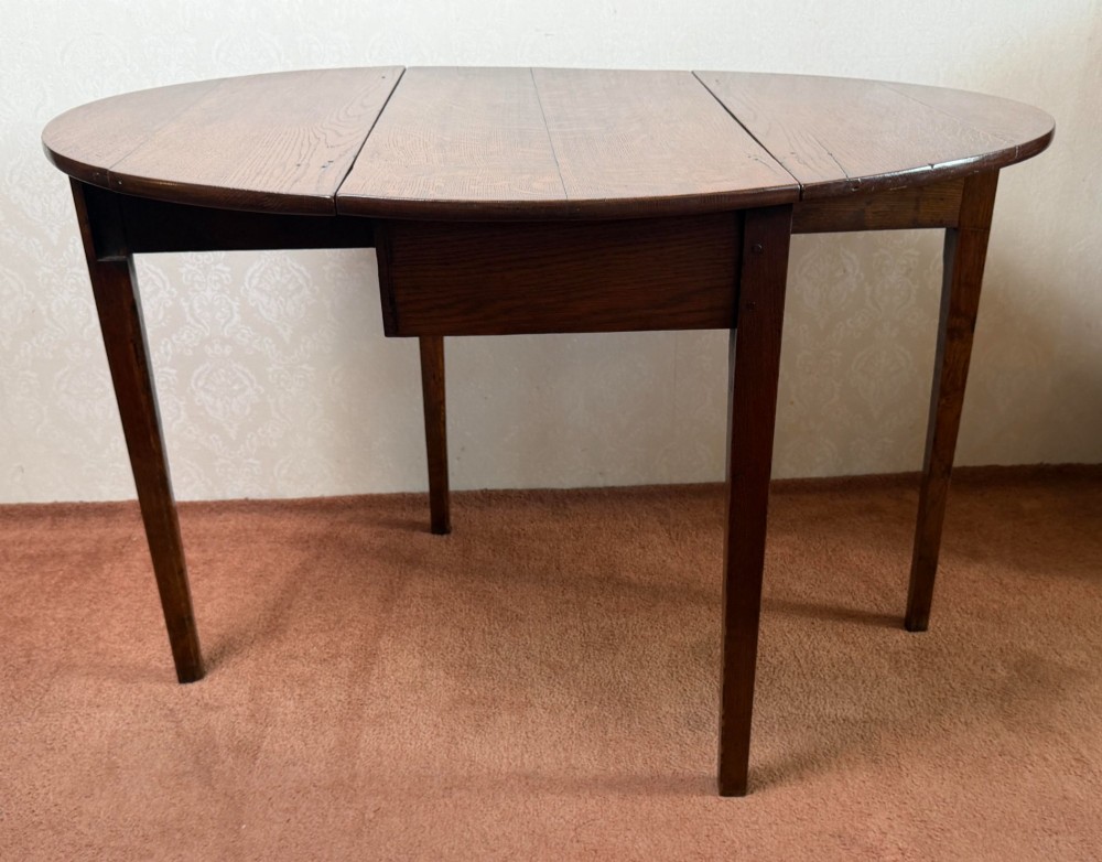 An antique warm brown oak drop leaf table with two folded oval leaves supported by four square legs. View II
