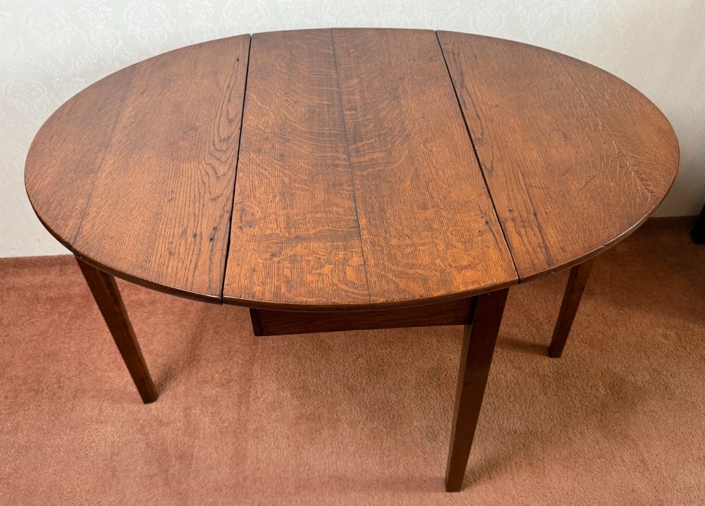 An antique warm brown oak drop leaf table with two folded oval leaves supported by four square legs. View III