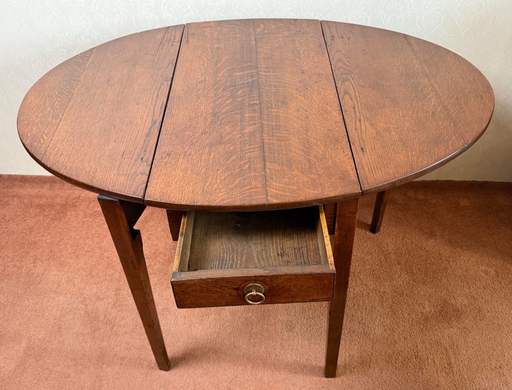 An antique warm brown oak drop leaf table with two folded oval leaves supported by four square legs. View IV