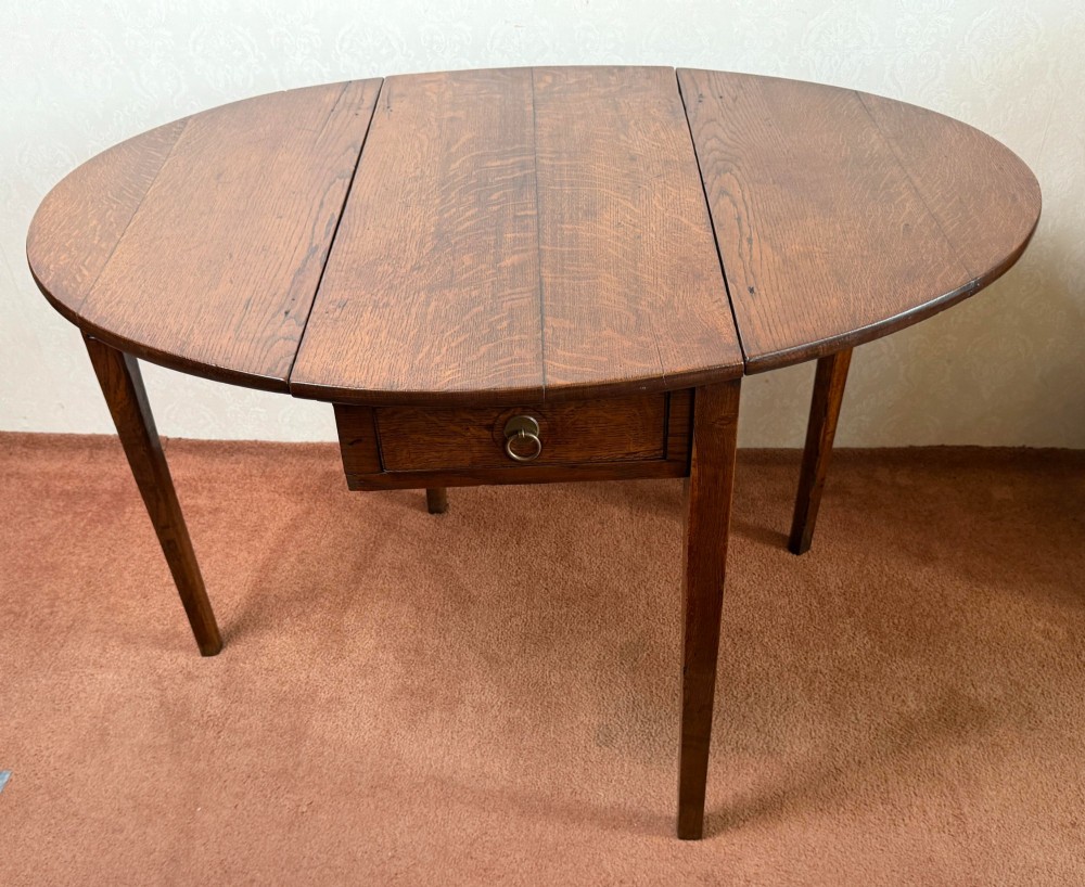 An antique warm brown oak drop leaf table with two folded oval leaves supported by four square legs. View V