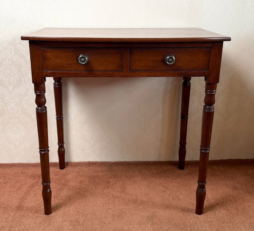 A mahogany bow front side table with two drawers, brass knobs, and slender turned legs.