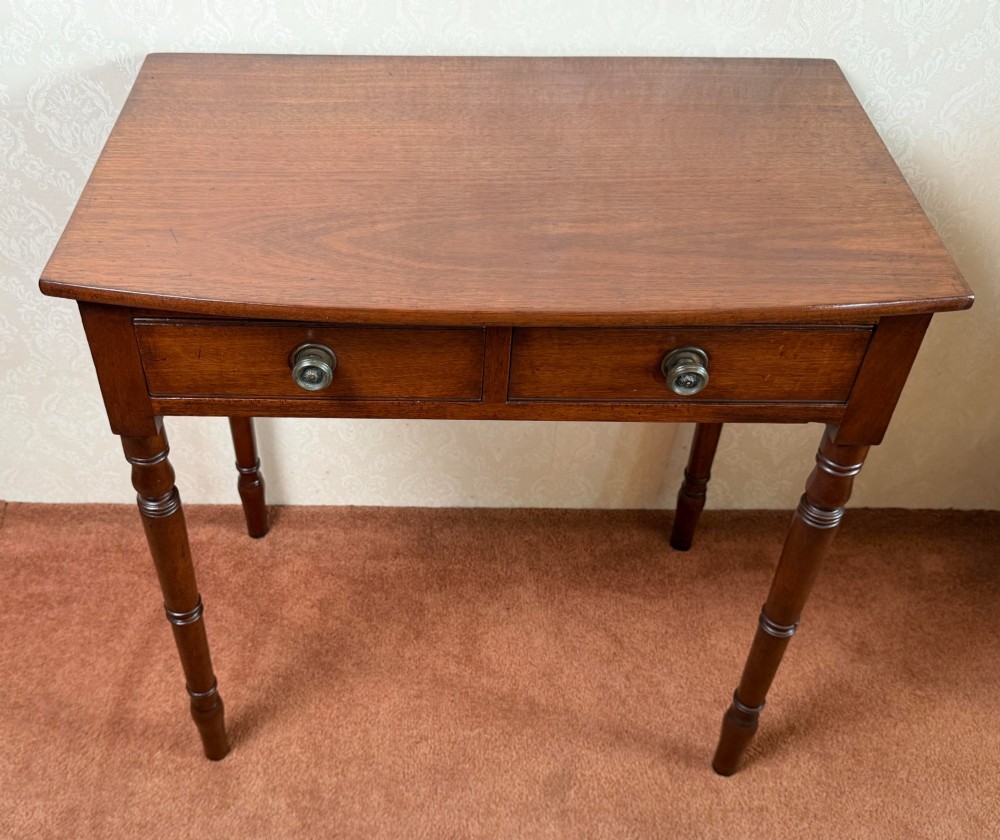 A mahogany bow front side table with two drawers, brass knobs, and slender turned legs. View II