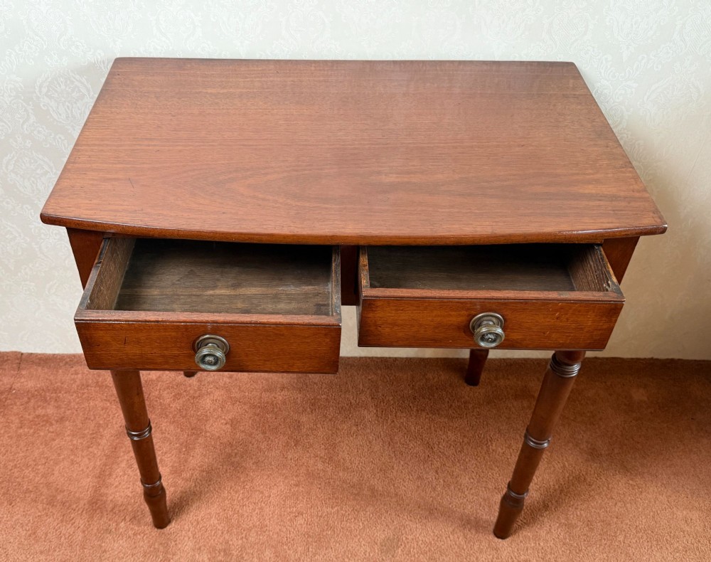 A mahogany bow front side table with two drawers, brass knobs, and slender turned legs. View III