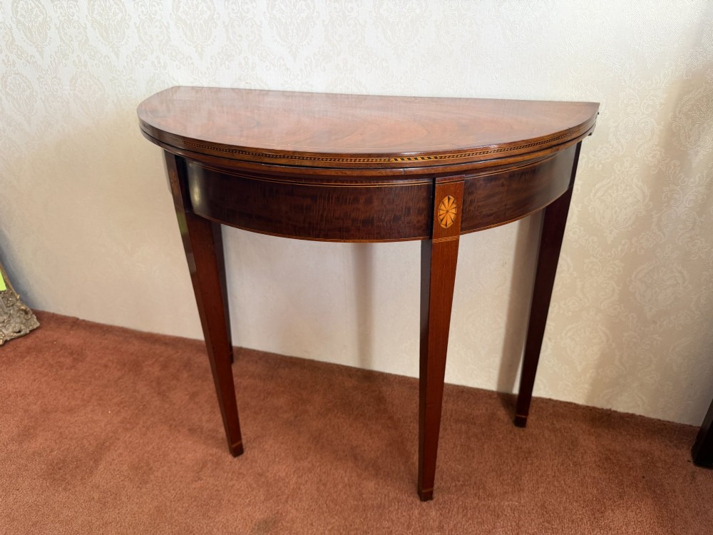 An 18th-century mahogany demi-lune card table featuring tapered legs, inlaid satinwood stringing, and a hinged fold-over top.