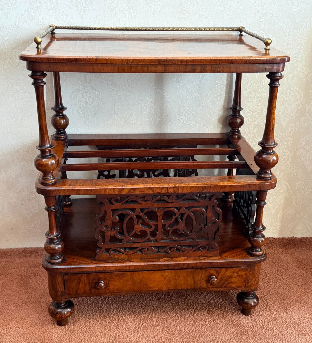 A Victorian burr walnut music Canterbury featuring a upper brass gallery rail, open vertical partitions with fretwork panels, turned corner columns, and a base drawer.
