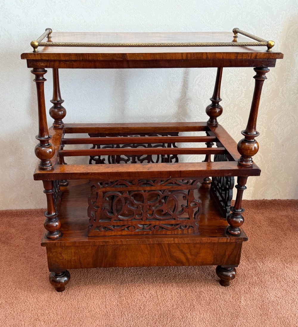 A Victorian burr walnut music Canterbury featuring a upper brass gallery rail, open vertical partitions with fretwork panels, turned corner columns, and a base drawer. View V
