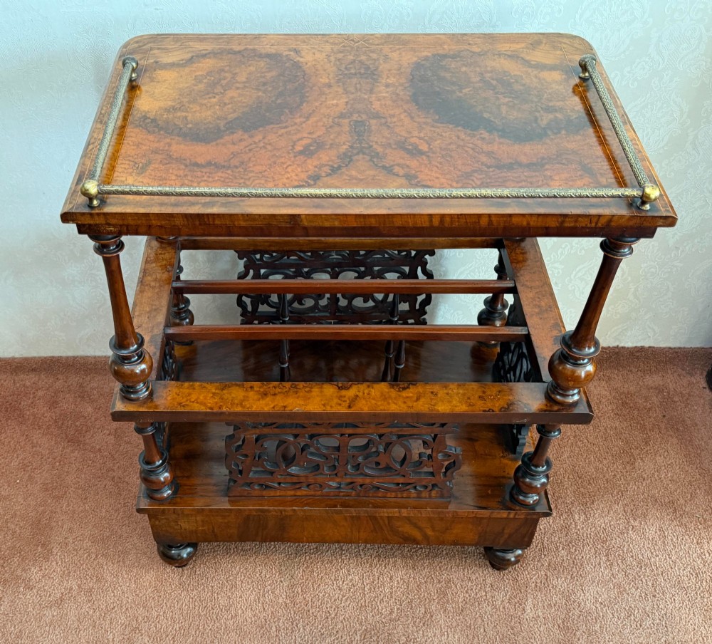 A Victorian burr walnut music Canterbury featuring a upper brass gallery rail, open vertical partitions with fretwork panels, turned corner columns, and a base drawer. View VI
