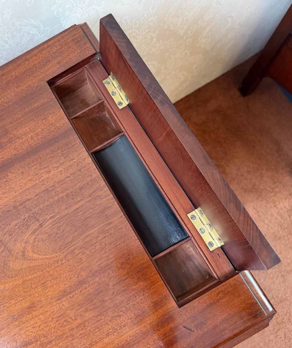 An antique Regency mahogany work table featuring a carved acanthus pedestal column, quadruped splayed legs with brass paw castors, and a hinged lid revealing a fitted compartment. View II