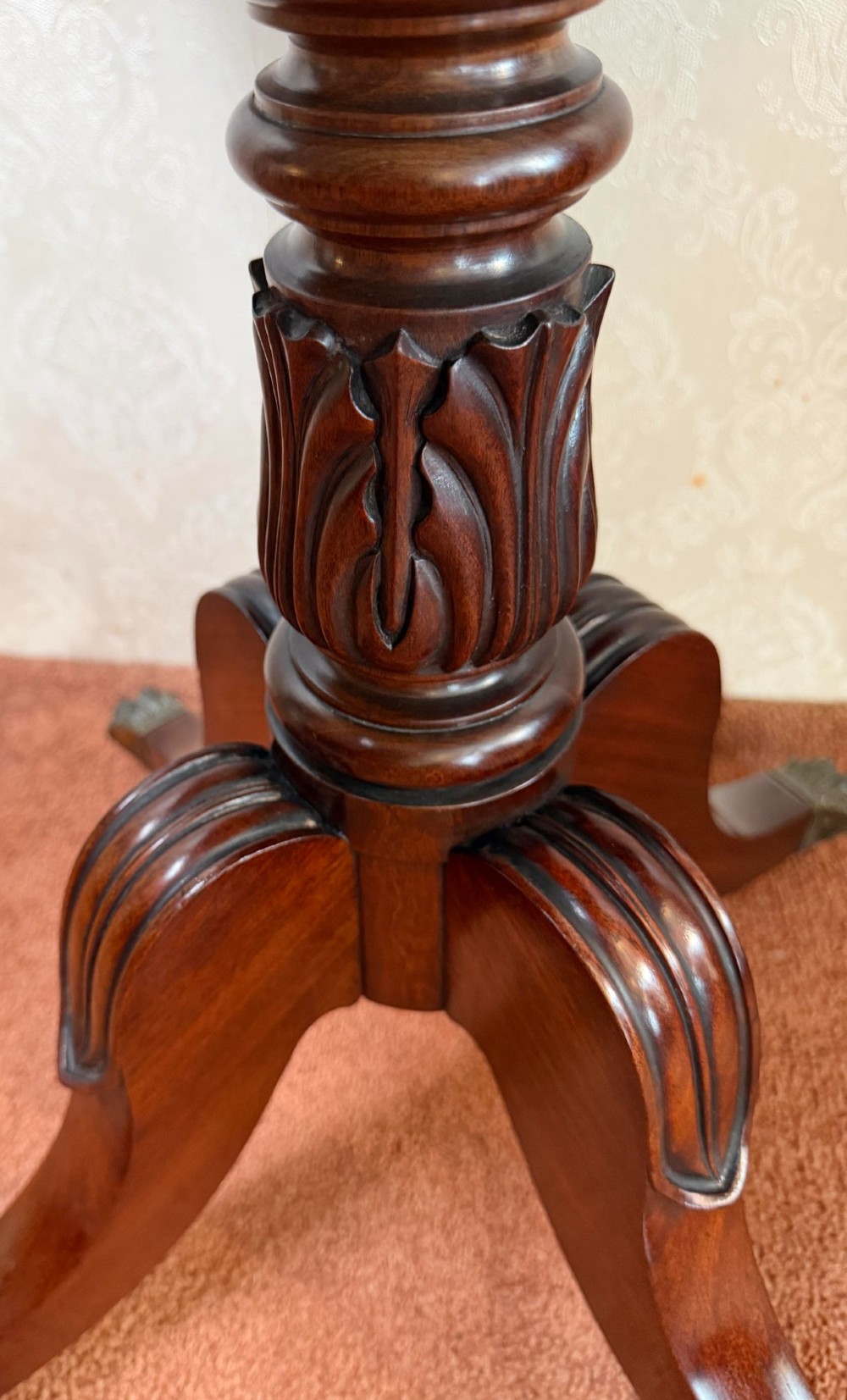 An antique Regency mahogany work table featuring a carved acanthus pedestal column, quadruped splayed legs with brass paw castors, and a hinged lid revealing a fitted compartment. View IV