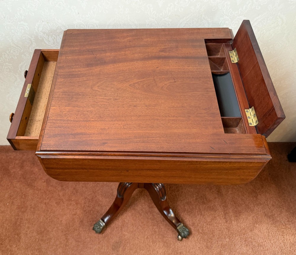 An antique Regency mahogany work table featuring a carved acanthus pedestal column, quadruped splayed legs with brass paw castors, and a hinged lid revealing a fitted compartment. View V