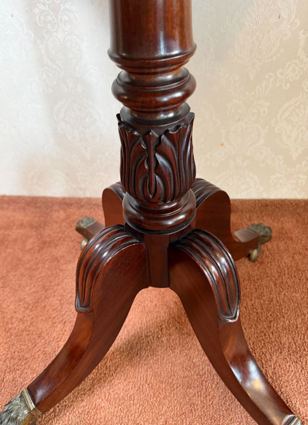 An antique Regency mahogany work table featuring a carved acanthus pedestal column, quadruped splayed legs with brass paw castors, and a hinged lid revealing a fitted compartment. View VII