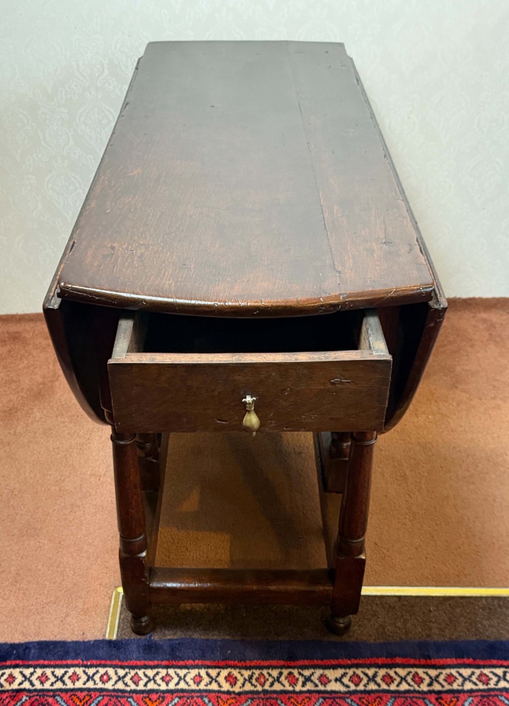 A 17th-century dark oak gateleg table shown with drop leaves lowered, featuring turned legs, a stretcher base, and a drawer with a brass teardrop pull handle. View III