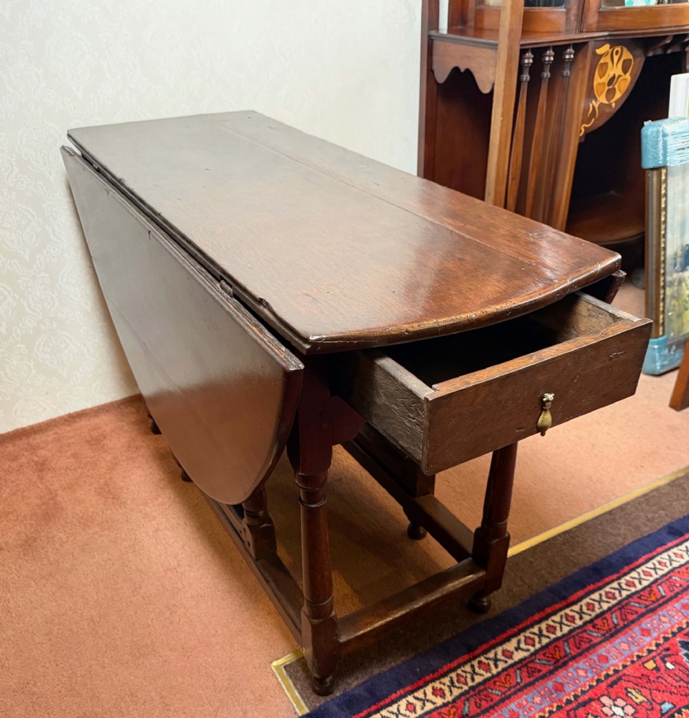 A 17th-century dark oak gateleg table shown with drop leaves lowered, featuring turned legs, a stretcher base, and a drawer with a brass teardrop pull handle. View IV