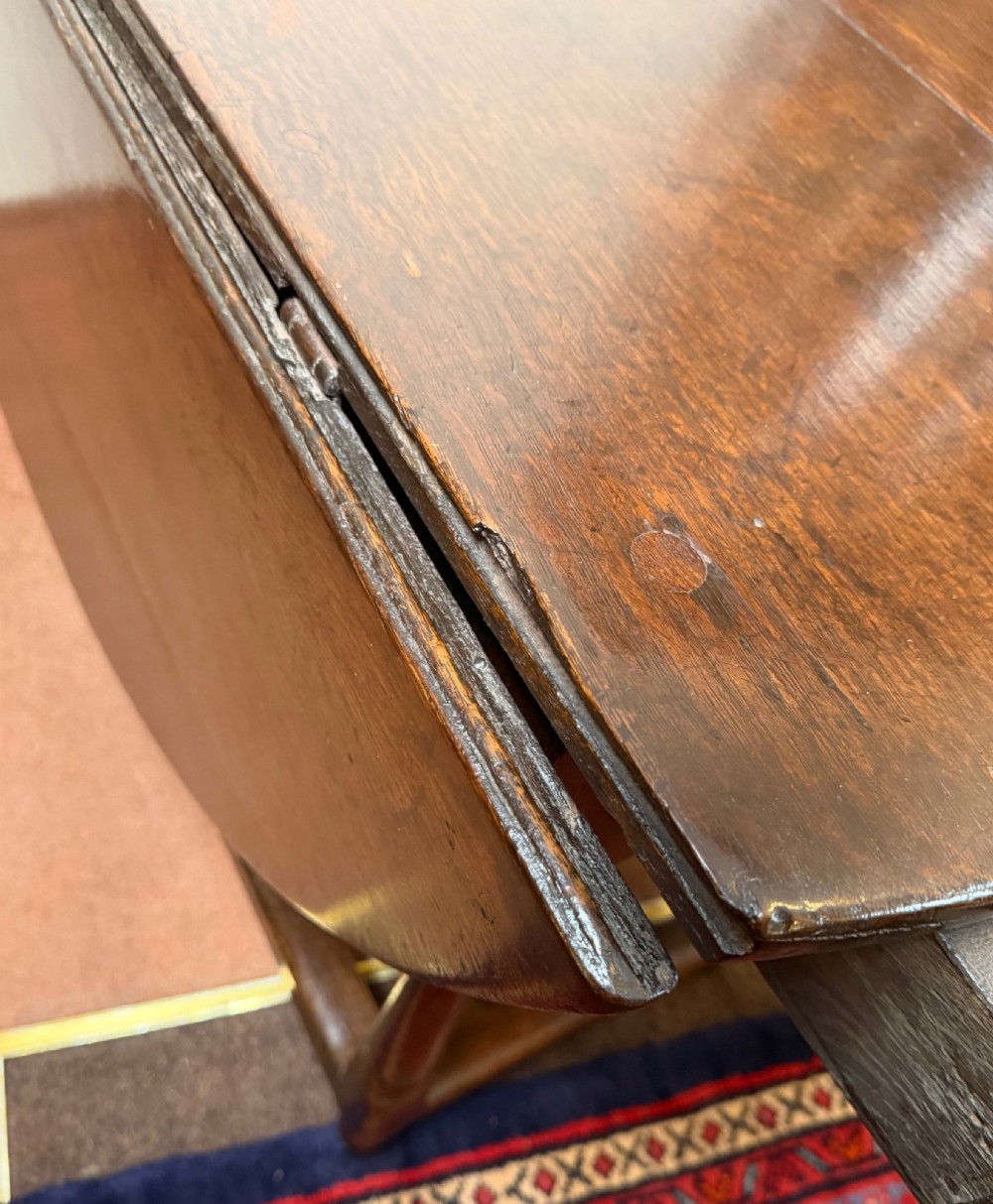 A 17th-century dark oak gateleg table shown with drop leaves lowered, featuring turned legs, a stretcher base, and a drawer with a brass teardrop pull handle. View V