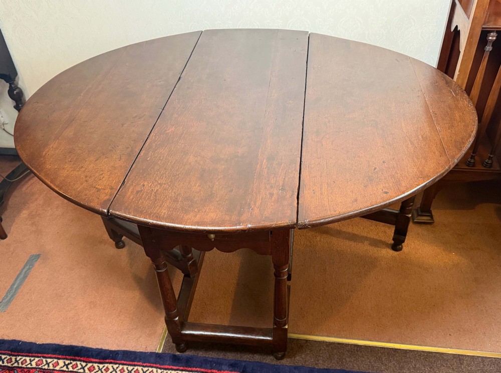 A 17th-century dark oak gateleg table shown with drop leaves lowered, featuring turned legs, a stretcher base, and a drawer with a brass teardrop pull handle. View VIII