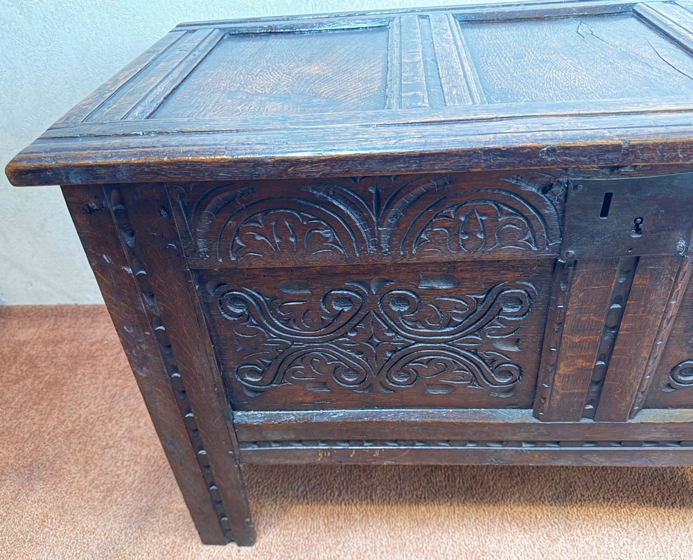 A seventeenth-century dark oak coffer with a panelled top, carved foliage front panels, carved frieze, and a wrought iron lockplate. View II