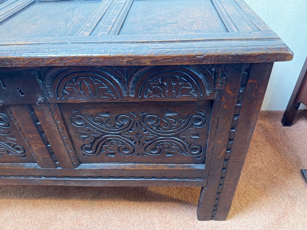 A seventeenth-century dark oak coffer with a panelled top, carved foliage front panels, carved frieze, and a wrought iron lockplate. View III