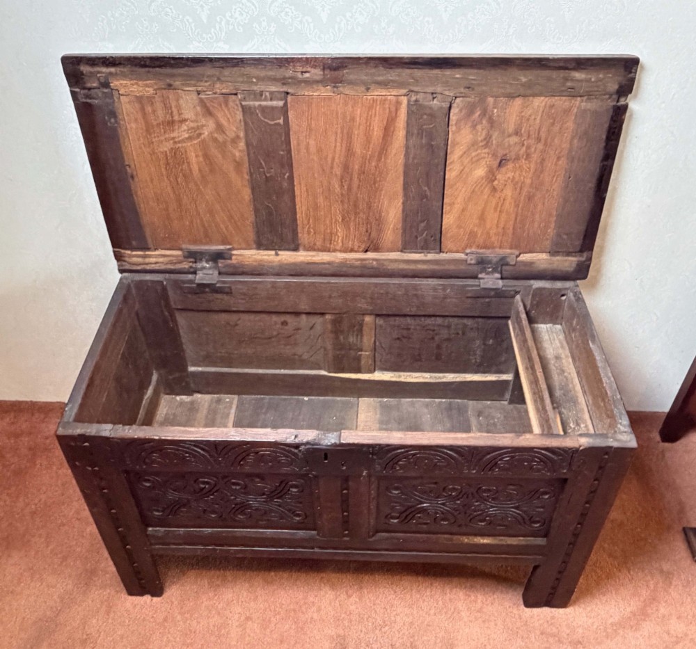 A seventeenth-century dark oak coffer with a panelled top, carved foliage front panels, carved frieze, and a wrought iron lockplate. View VI