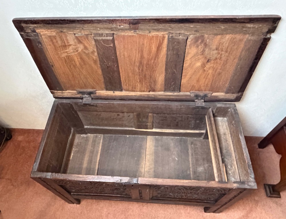 A seventeenth-century dark oak coffer with a panelled top, carved foliage front panels, carved frieze, and a wrought iron lockplate. View VII