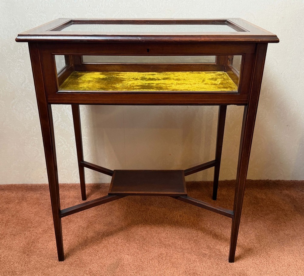 A late 19th-century mahogany bijouterie table featuring glass top and side panels, a yellow velvet-lined display interior, tapered square legs, and an X-shaped stretcher with a central undertier.
