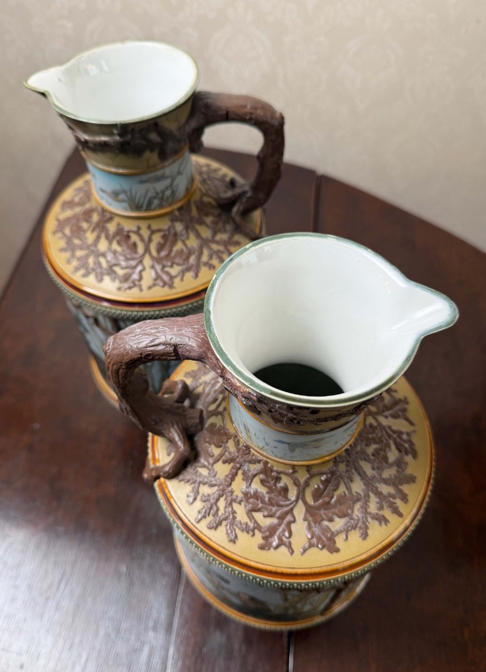 A pair of 19th-century Mettlach stoneware vases featuring sculpted branch handles, oak leaf relief decoration, and incised pictorial hunting scenes in blue and brown. View IV