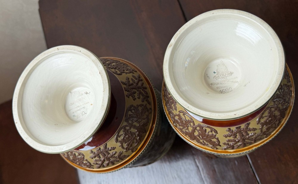 A pair of 19th-century Mettlach stoneware vases featuring sculpted branch handles, oak leaf relief decoration, and incised pictorial hunting scenes in blue and brown. View VIII