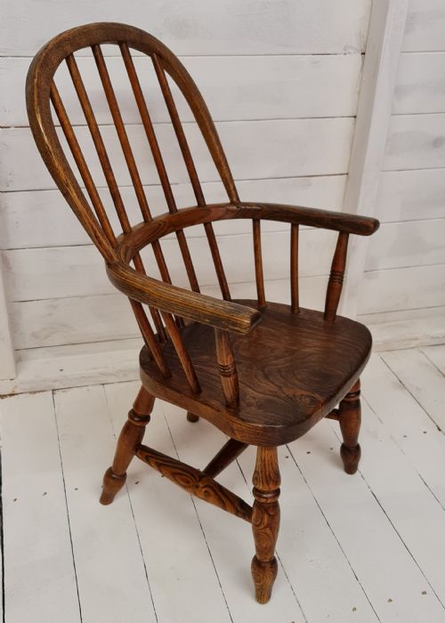 fig 1. A 19th-century childs Windsor armchair crafted from warm brown ash and elm timber, featuring a hoop spindle back, shaped saddle seat, and turned legs.