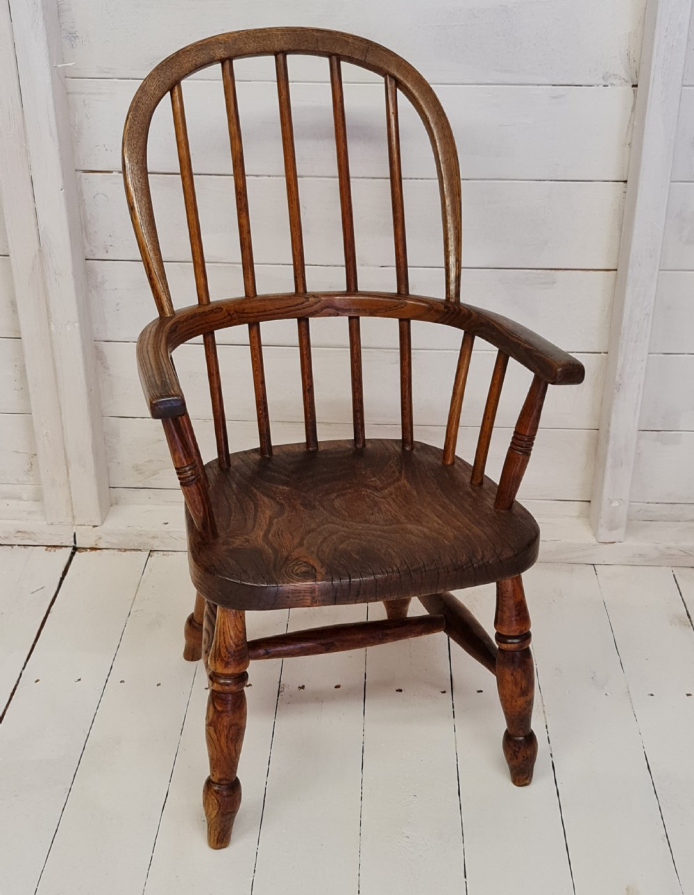 A 19th-century childs Windsor armchair crafted from warm brown ash and elm timber, featuring a hoop spindle back, shaped saddle seat, and turned legs.