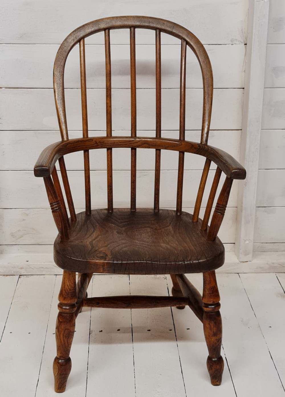 A 19th-century childs Windsor armchair crafted from warm brown ash and elm timber, featuring a hoop spindle back, shaped saddle seat, and turned legs. View III