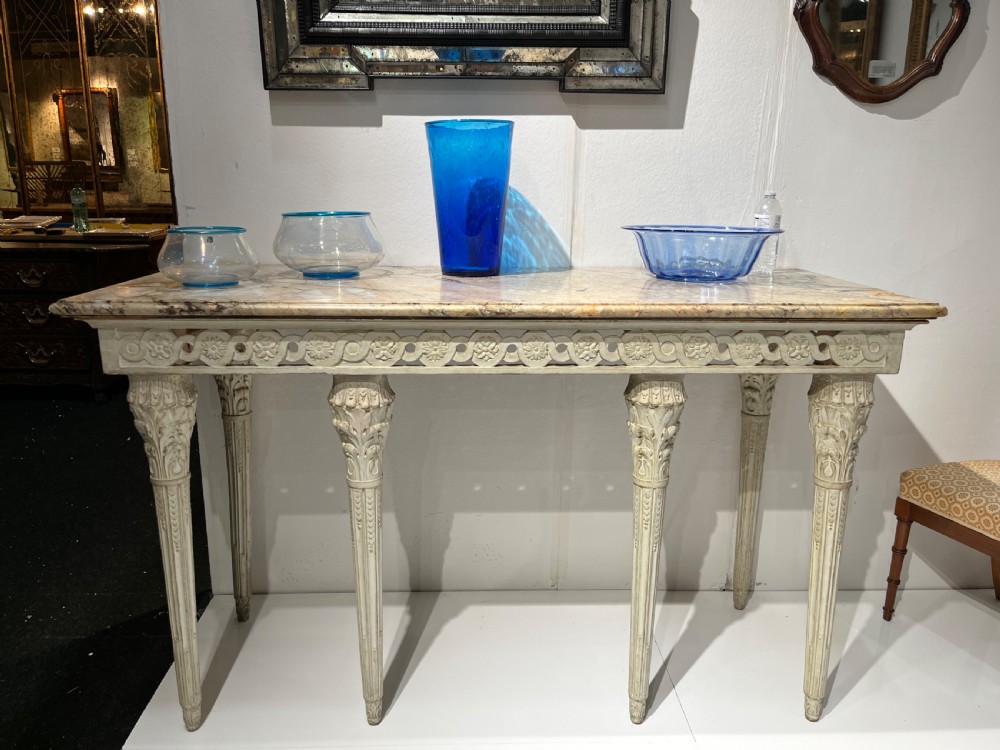 An Italian Neoclassical cream-painted console table featuring a marble top, pierced frieze with rosette carving, and four tapered fluted legs. View III