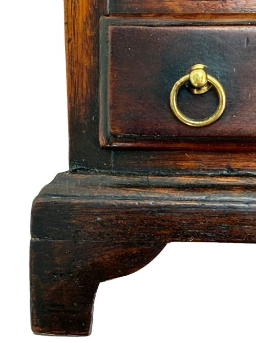 fig 2. A miniature 18th-century mahogany chest of drawers featuring two small drawers over three long drawers with brass ring drop handles and bracket feet.