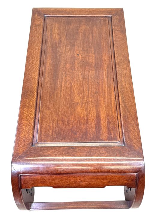 fig 1. A low dark hardwood coffee table featuring an openwork carved apron and inward-curving scroll legs.