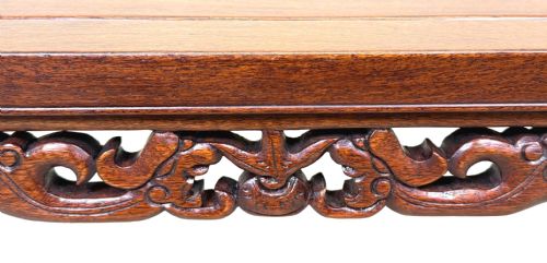 fig 2. A low dark hardwood coffee table featuring an openwork carved apron and inward-curving scroll legs.