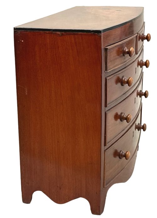 fig 1. A Regency miniature mahogany bowfront chest featuring two short over three long graduated drawers with turned wooden knobs and brass keyhole escutcheons.