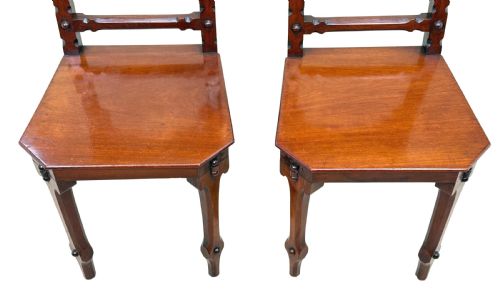 fig 1. A pair of Victorian mahogany hall chairs featuring carved shield backrests, open architectural arches, turned finials, and solid wooden seats.