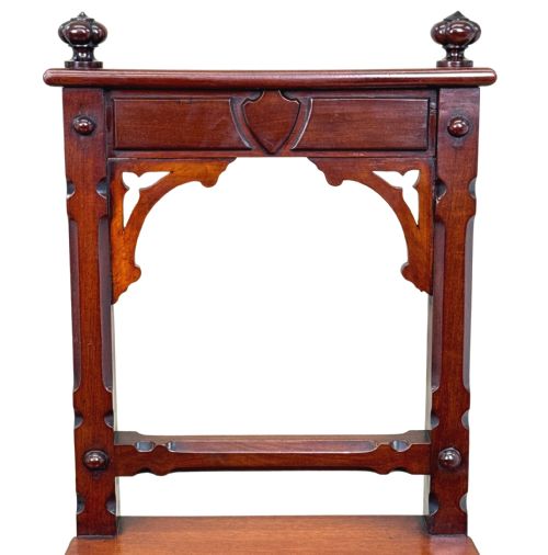 fig 4. A pair of Victorian mahogany hall chairs featuring carved shield backrests, open architectural arches, turned finials, and solid wooden seats.