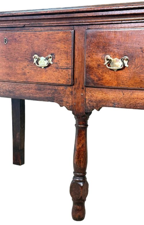 fig 1. An early eighteenth-century oak dresser base featuring three drawers with brass drop handles, brass keyhole escutcheons, turned front legs, and a dark brown finish.