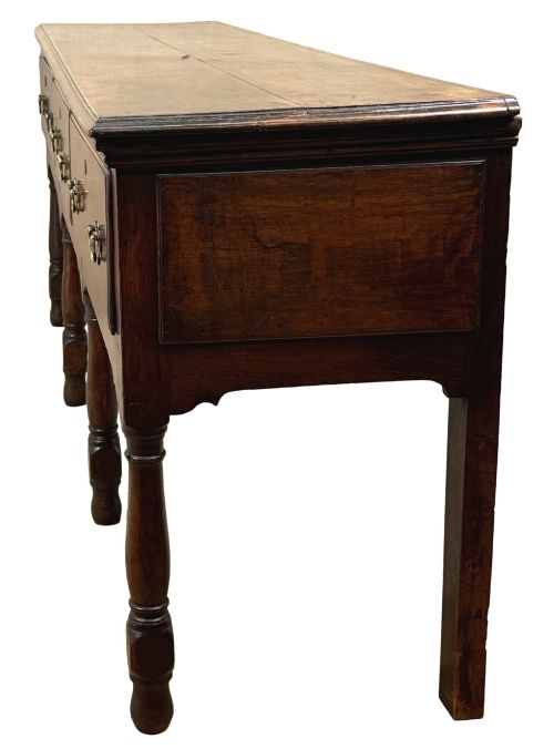 fig 2. An early eighteenth-century oak dresser base featuring three drawers with brass drop handles, brass keyhole escutcheons, turned front legs, and a dark brown finish.