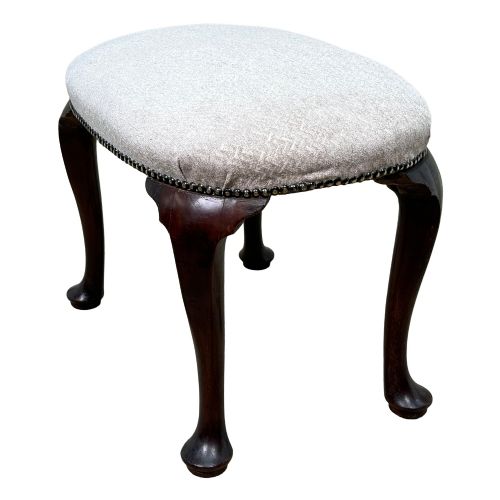 fig 1. An early 18th-century George I walnut stool featuring an oval light grey upholstered seat trimmed with metal studs above four cabriole legs ending in pad feet.