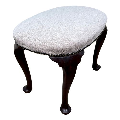 fig 3. An early 18th-century George I walnut stool featuring an oval light grey upholstered seat trimmed with metal studs above four cabriole legs ending in pad feet.