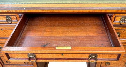 fig 1. A mid-19th-century English birdseye maple pedestal desk featuring a green leather writing surface, multiple drawers with brass ring drop handles, and a plinth base.