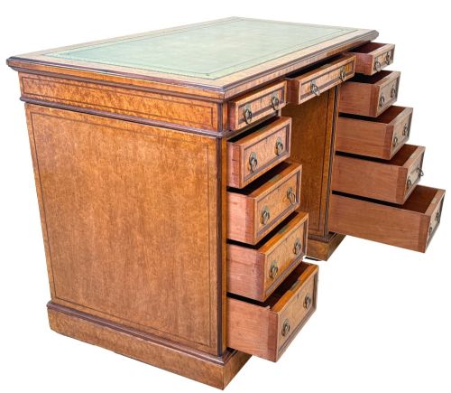 fig 3. A mid-19th-century English birdseye maple pedestal desk featuring a green leather writing surface, multiple drawers with brass ring drop handles, and a plinth base.