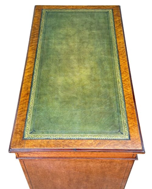 fig 4. A mid-19th-century English birdseye maple pedestal desk featuring a green leather writing surface, multiple drawers with brass ring drop handles, and a plinth base.