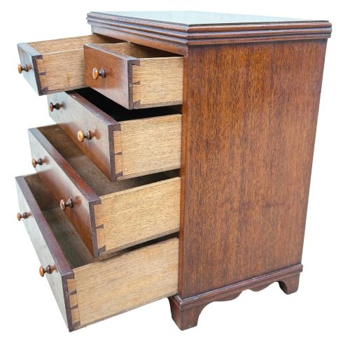 fig 1. A miniature early nineteenth-century mahogany chest of drawers with two short over three long graduated drawers, turned wooden knobs, and a shaped apron base.