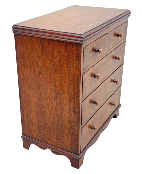 fig 2. A miniature early nineteenth-century mahogany chest of drawers with two short over three long graduated drawers, turned wooden knobs, and a shaped apron base.