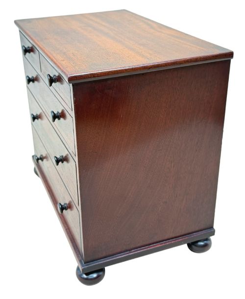 fig 1. A mid-nineteenth-century miniature mahogany chest of drawers featuring two short over three long drawers, turned dark knobs, and bun feet.