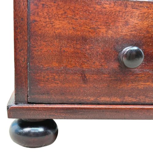 fig 2. A mid-nineteenth-century miniature mahogany chest of drawers featuring two short over three long drawers, turned dark knobs, and bun feet.