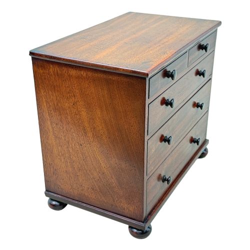 fig 4. A mid-nineteenth-century miniature mahogany chest of drawers featuring two short over three long drawers, turned dark knobs, and bun feet.